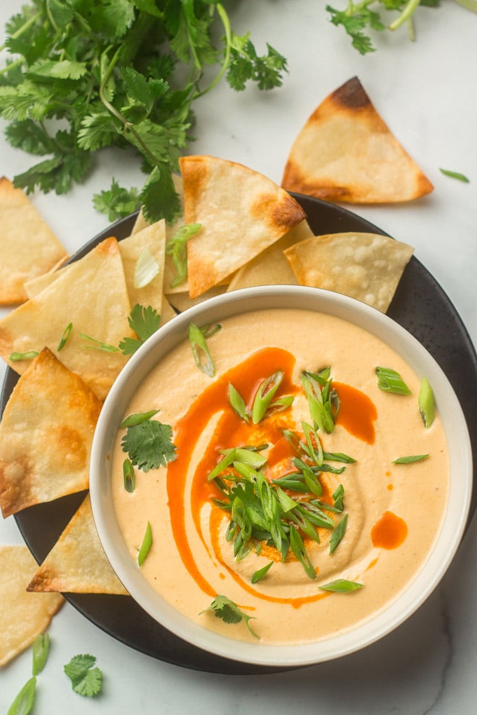 Bowl of Cashew Queso Topped with Scallions, Cilantro and Hot Sauce, and Surrounded by Chips