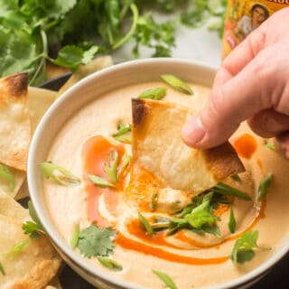 Hand Dipping a Chip in a Bowl of Cashew Queso