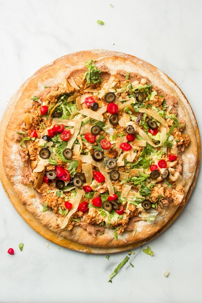 Unsliced Vegan Taco Pizza on a Pizza Stone on a Marble Background