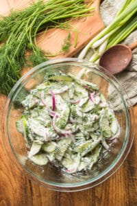 Wooden Table Set with a Bowl of Creamy Cucumber Dill Salad, Wooden Spoon, Fresh Dill and Scallions