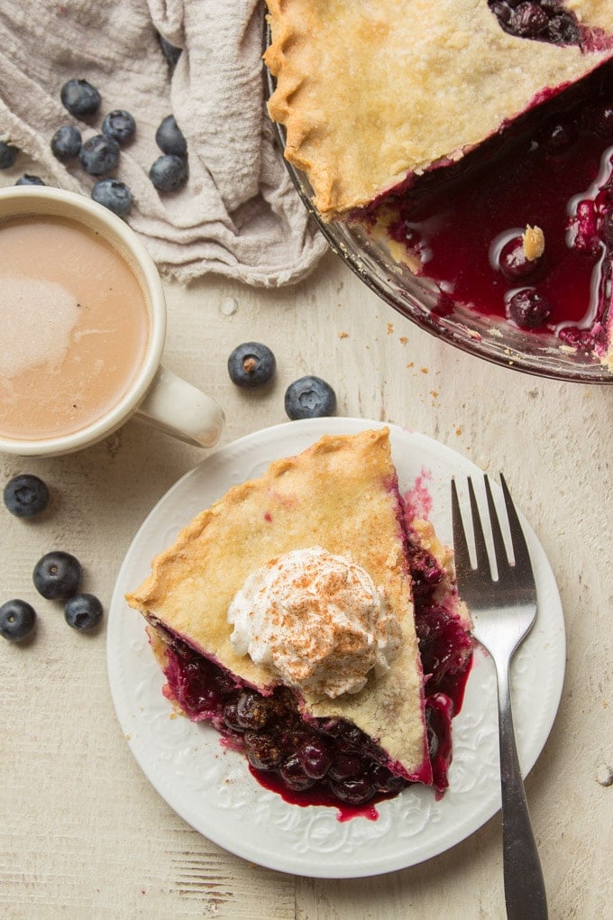 Overhead View of a Table Set with Vegan Blueberry Pie, Slice of Pie on a Plate, Fork, and Coffee Cup