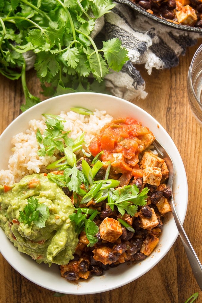 Tofu and Black Bean Burrito Bowl Topped with Salsa and Guacamole on a Wooden Surface