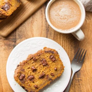 Wooden surface set with slice of pumpkin bread and cup of coffee.