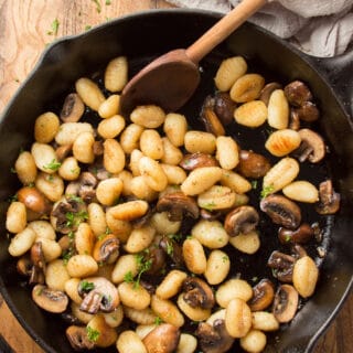 Cast Iron Skillet of Fried Gnocchi and Mushrooms on a Wooden Surface