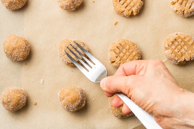 Hand Using a Fork To Flatten Balls of Vegan Peanut Butter Cookie Dough on a Baking Sheet