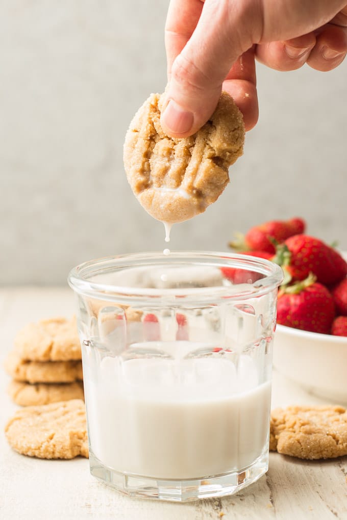 Hand Dipping a Vegan Peanut Butter Cookie in a Glass of Almond Milk