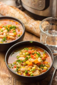Two Bowls of Instant Pot Vegetable Soup with Water Glass, Baguette, and Instant Pot in the Background