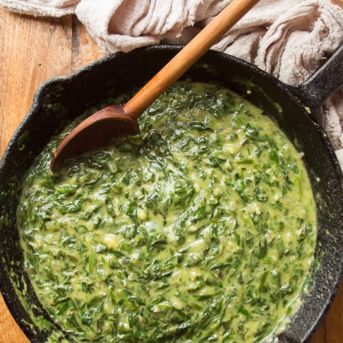 Cast Iron Skillet Sitting on a Wood Surface and Filled with Vegan Creamed Spinach with Wooden Spoon