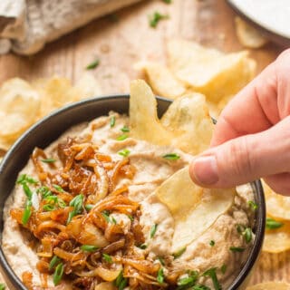 Hand Dipping a Chip into a Bowl of Vegan French Onion Dip