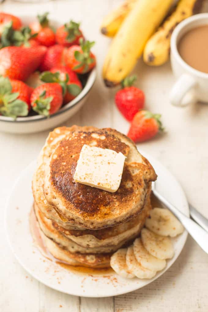 Plate of Vegan Banana Pancakes with Bowl of Strawberries, Bunch of Bananas and Coffee Cup in the Background