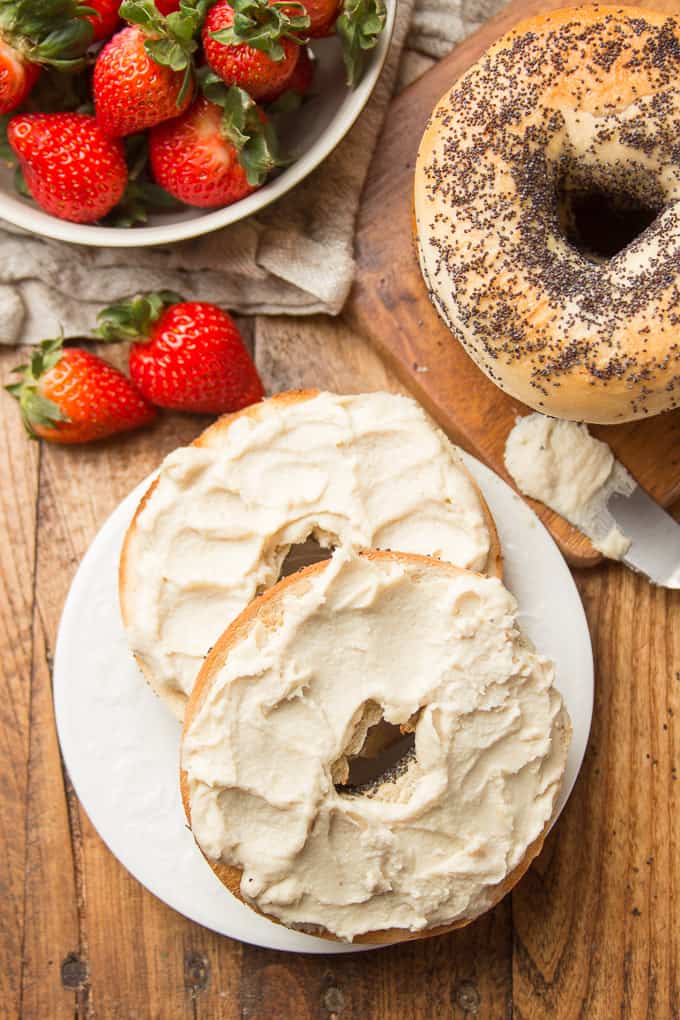 Wooden Table Set with Bowl of Strawberries, Bagels, and Two Bagel Halves on a Plate with Vegan Cream Cheese on Top