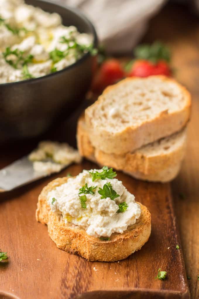 Toasted Baguette Slice Topped with Vegan Ricotta Cheese and Parsley with Bowl, Baguette Slices and Strawberries in the Background