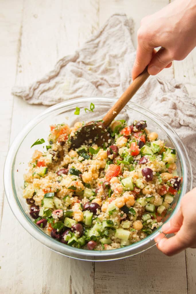 Hand Stirring Mediterranean Quinoa Salad in a Glass Mixing Bowl