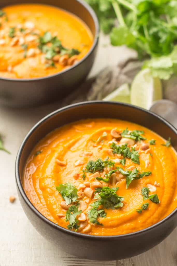 Two Bowls of Thai Carrot Soup with Lime Wedges and Cilantro in the Background