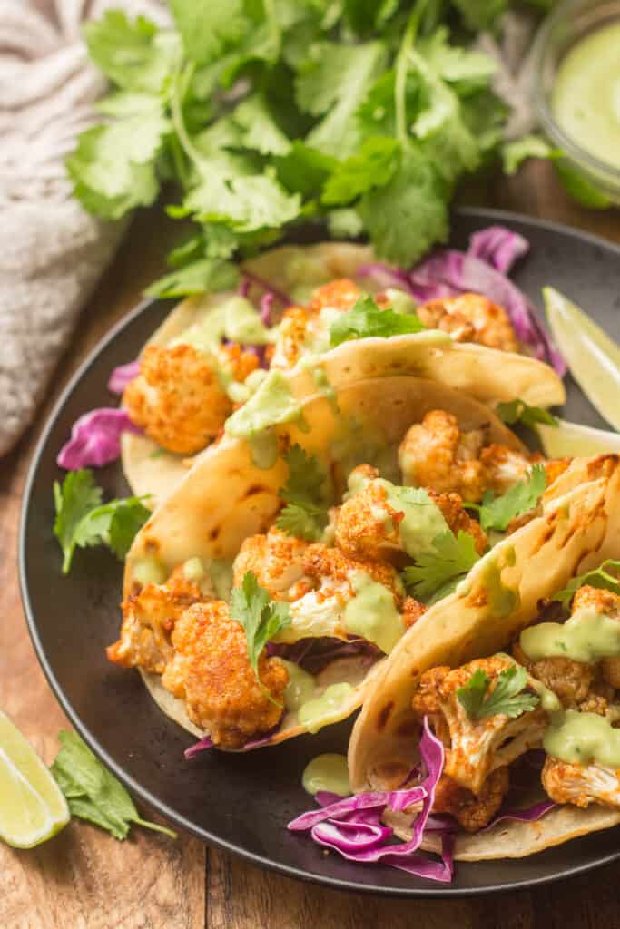 Tacos de coliflor en un plato con cilantro al fondo