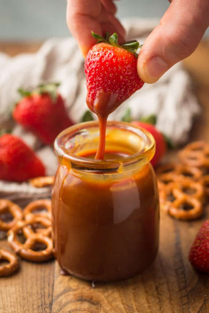 Hand Dipping a Strawberry in a Jar of Vegan Caramel Sauce
