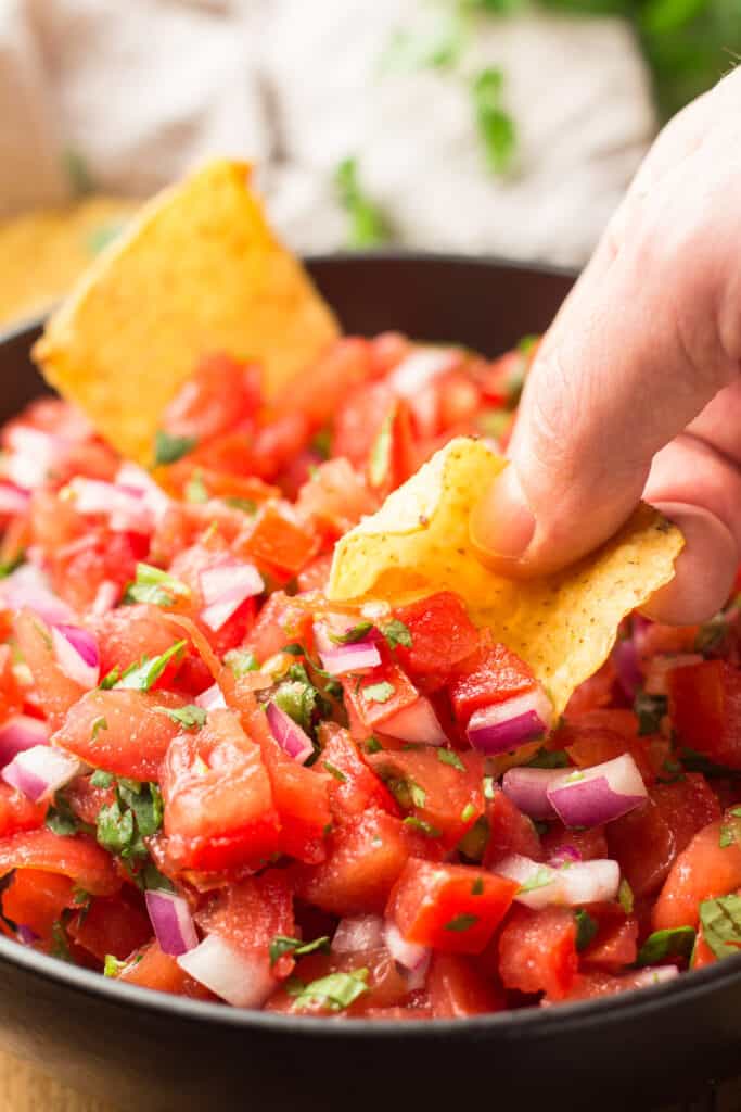 Close Up of Hand Dipping Chip in Pico de Gallo