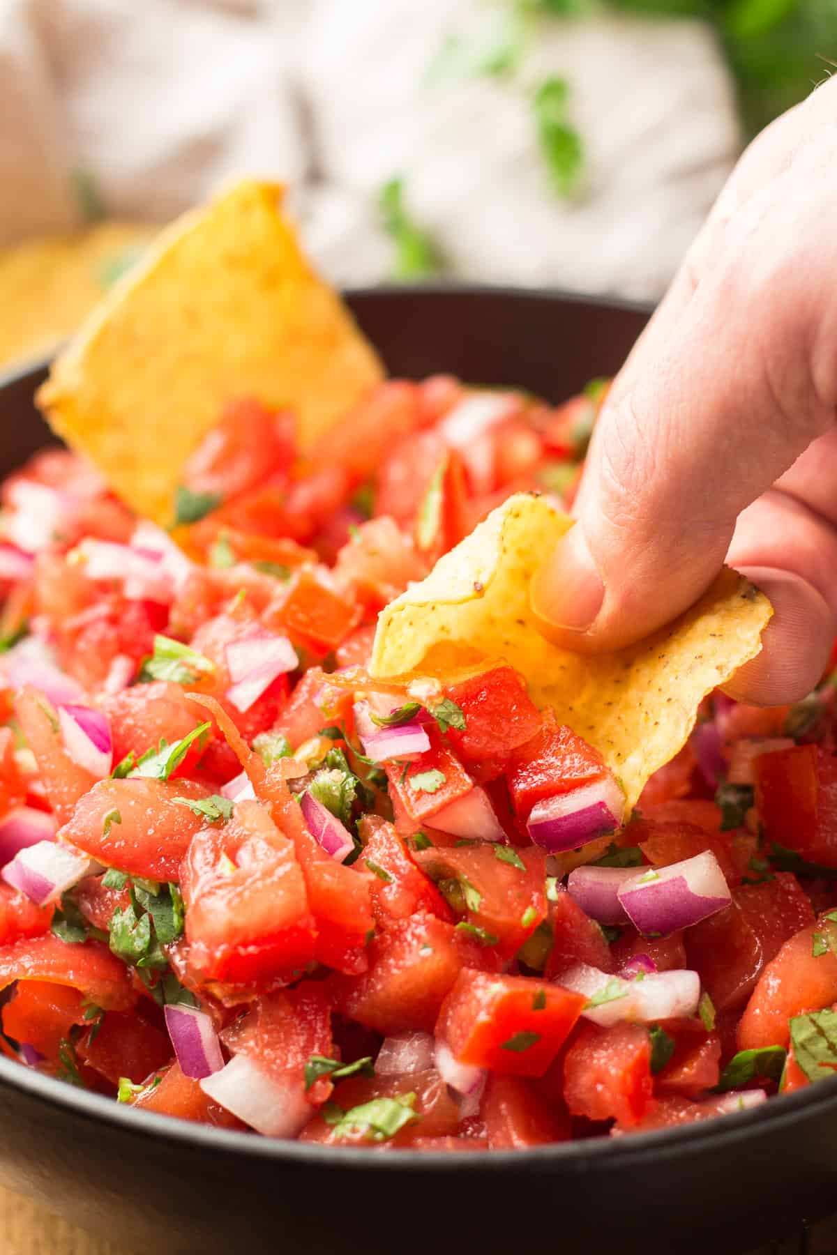 Close Up of Hand Dipping Chip in Pico de Gallo