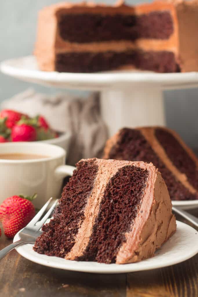 Rebanada de pastel de chocolate vegano en el lateral en un plato con un molde para pastel en el fondo