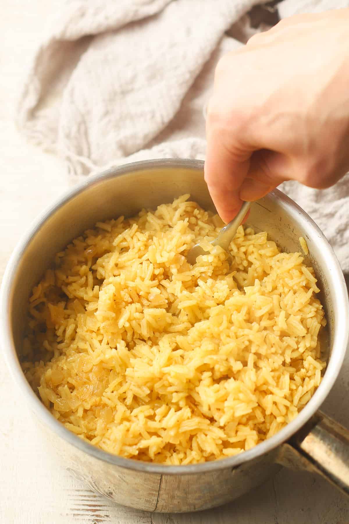 Esponja el arroz con cúrcuma a mano en una cacerola con un tenedor.