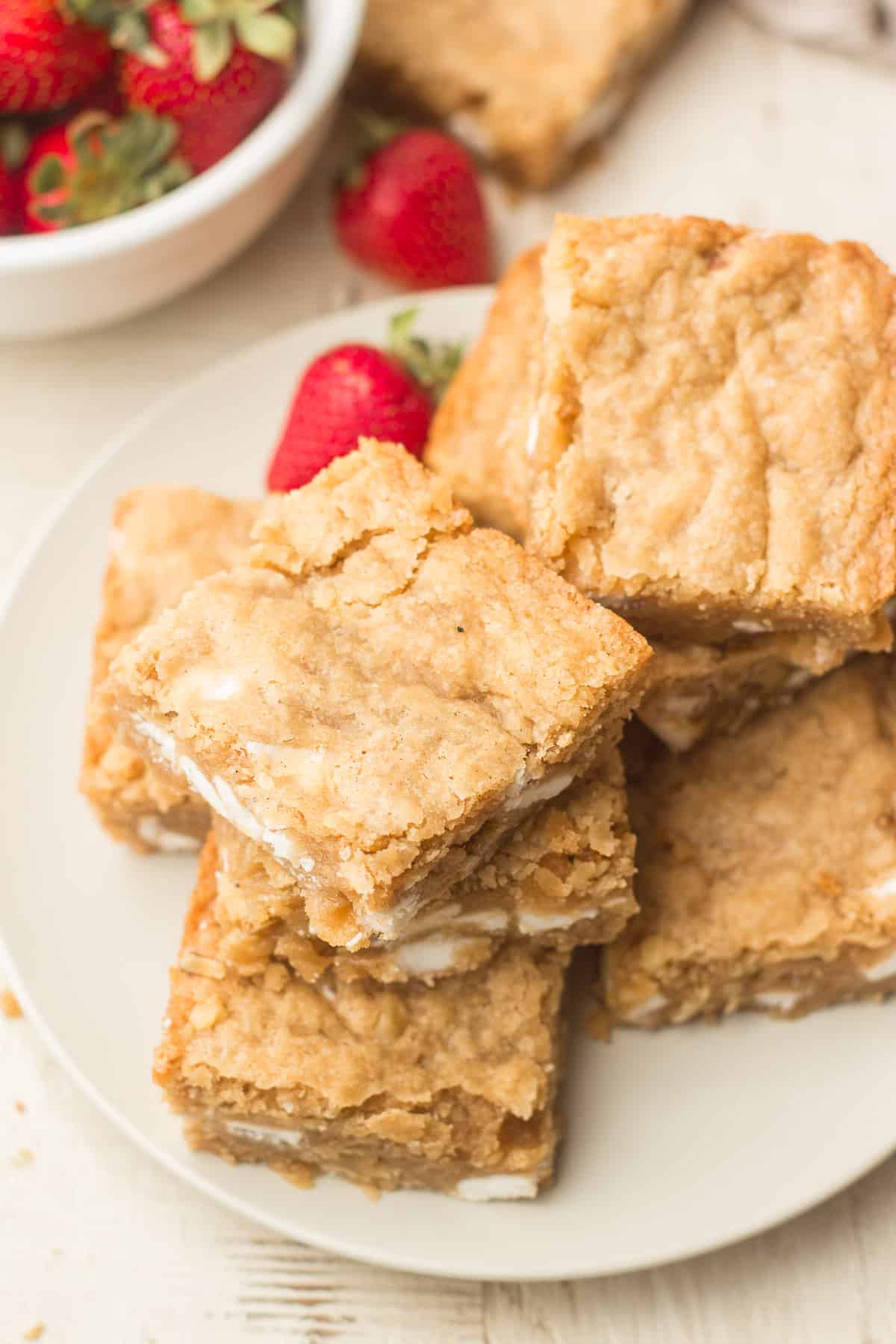 Plate of vegan blondies and strawberries, with a bowl of strawberries in the background
