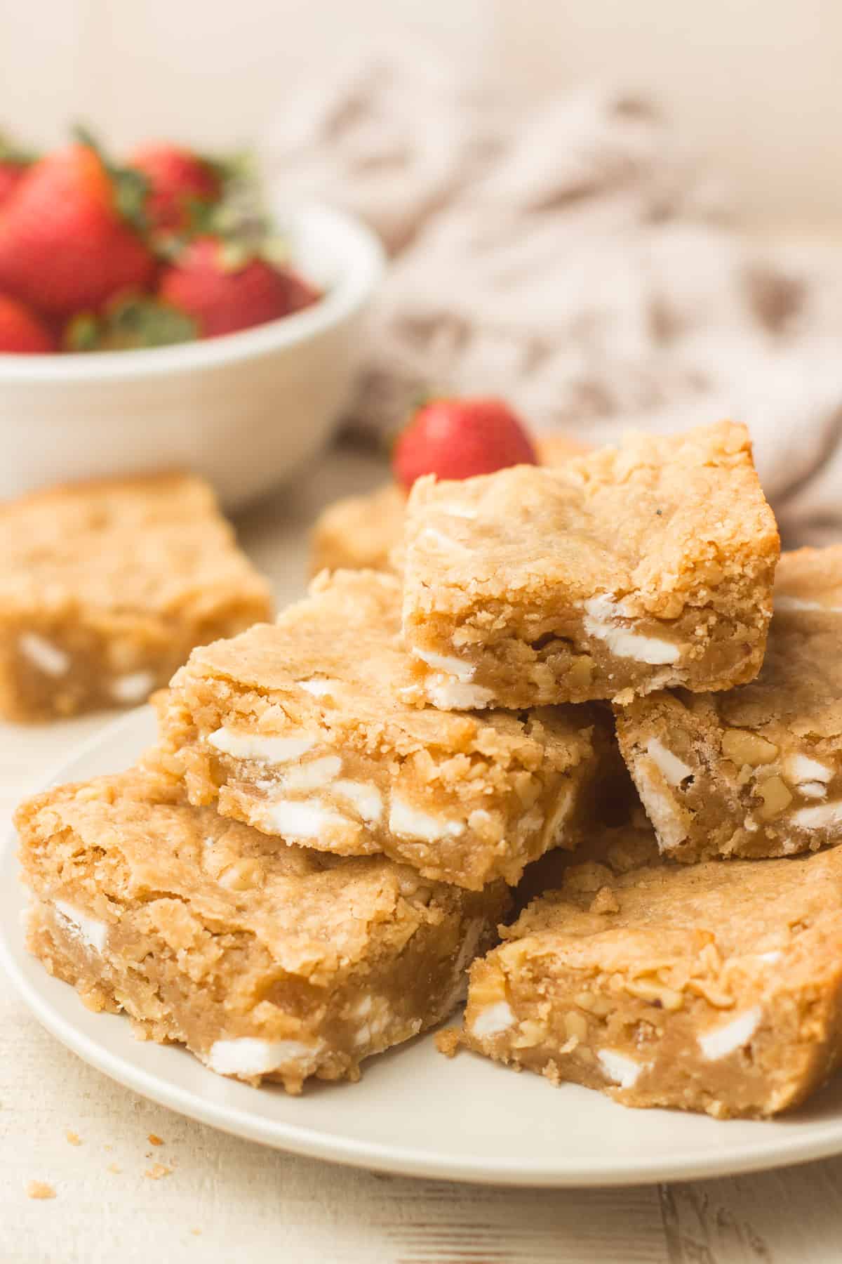 Vegan Blondies stacked on a plate with a bowl of strawberries in the background