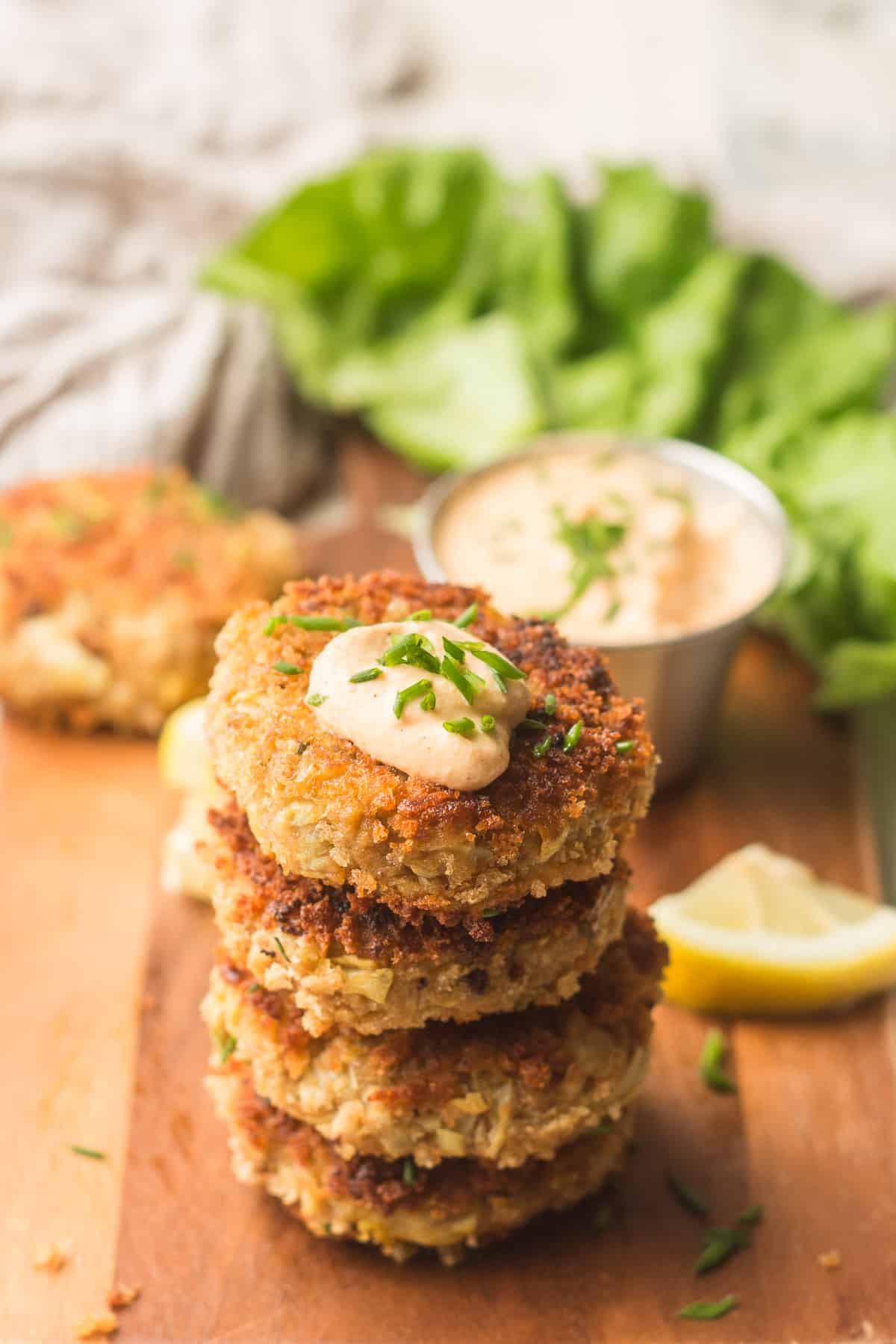Stack of Vegan Crab Cakes Lettuce Leaf, Lemon Wedge, and Dish of Aioli in the Background