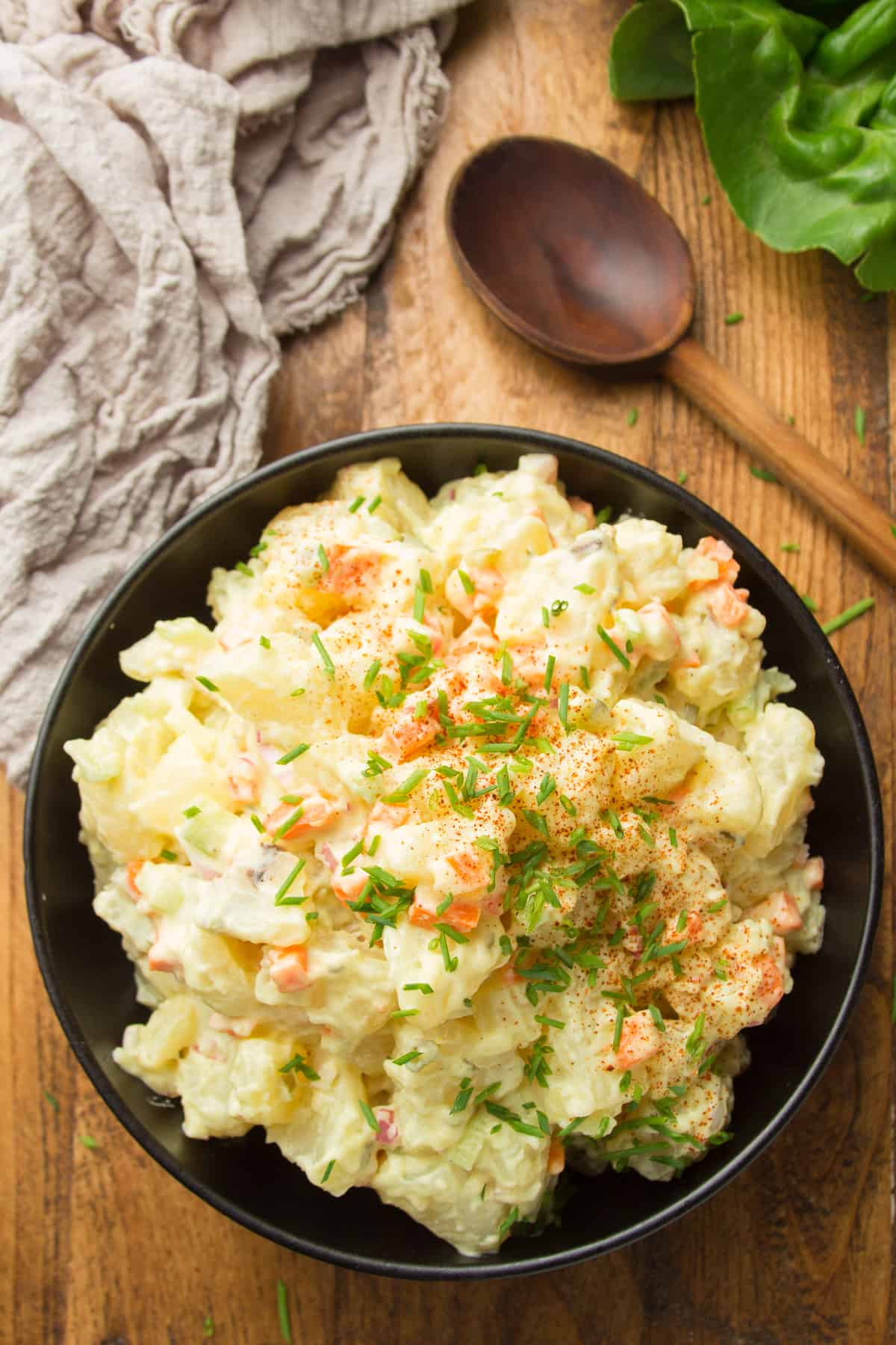 Bowl of Vegan Potato Salad on a Wooden Surface with Wooden Spoon on the Side