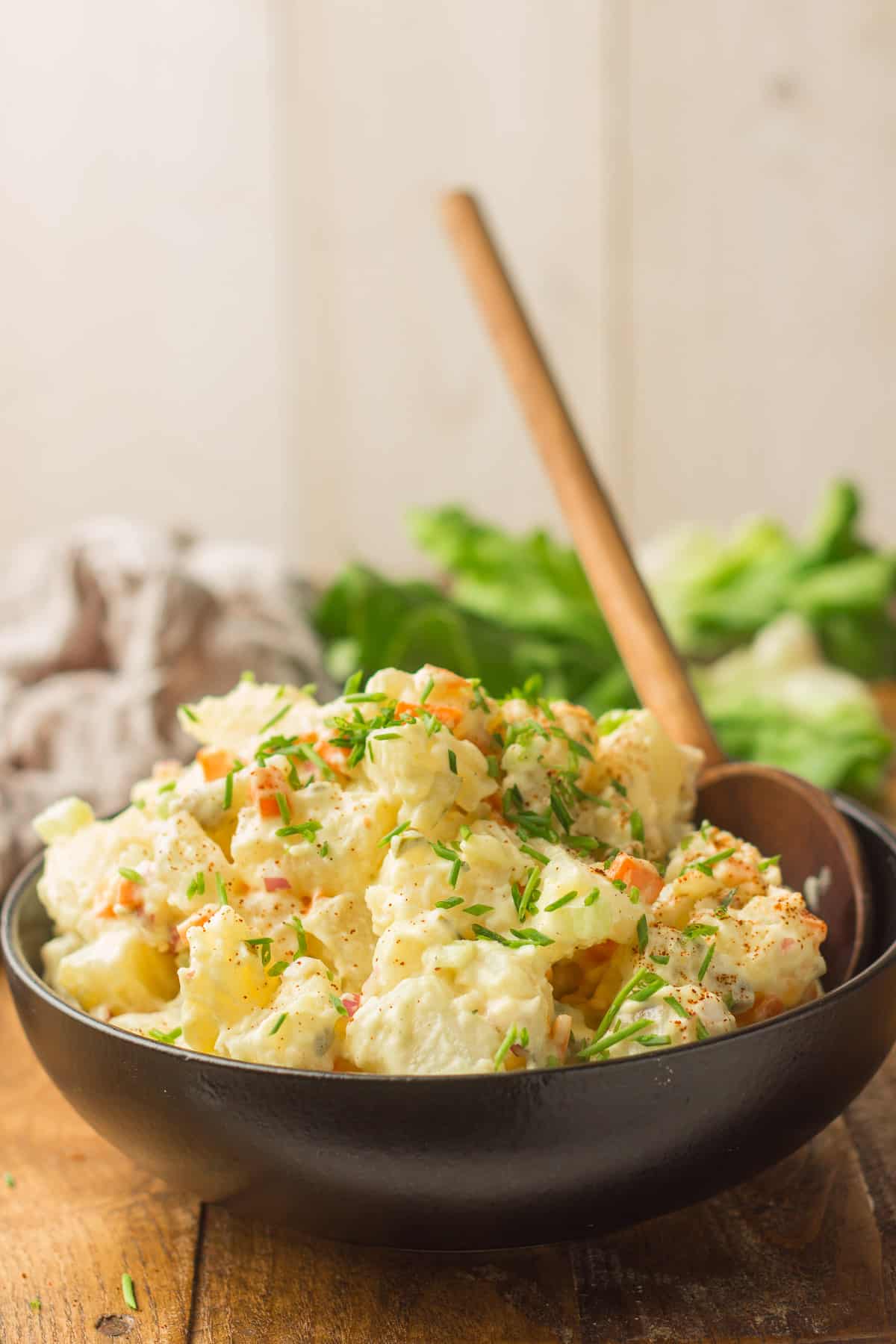 Bowl of Vegan Potato Salad with Wooden Spoon, with Napkin and Lettuce Leaves in the Background