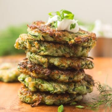Stack of vegan zucchini fritters with sour cream on top.
