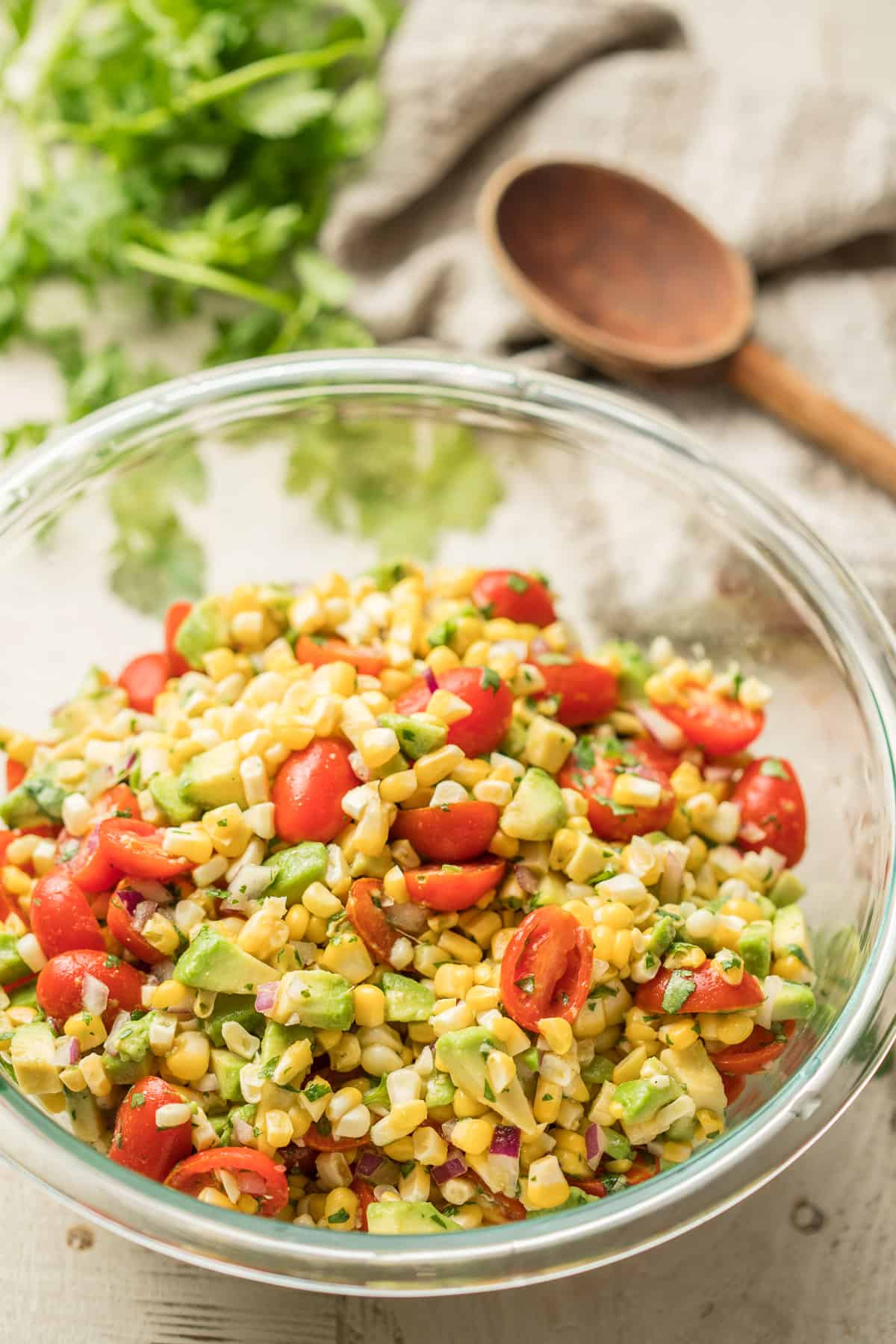 Glass Bowl of Avocado Corn Salad with Wooden Spoon in the Background