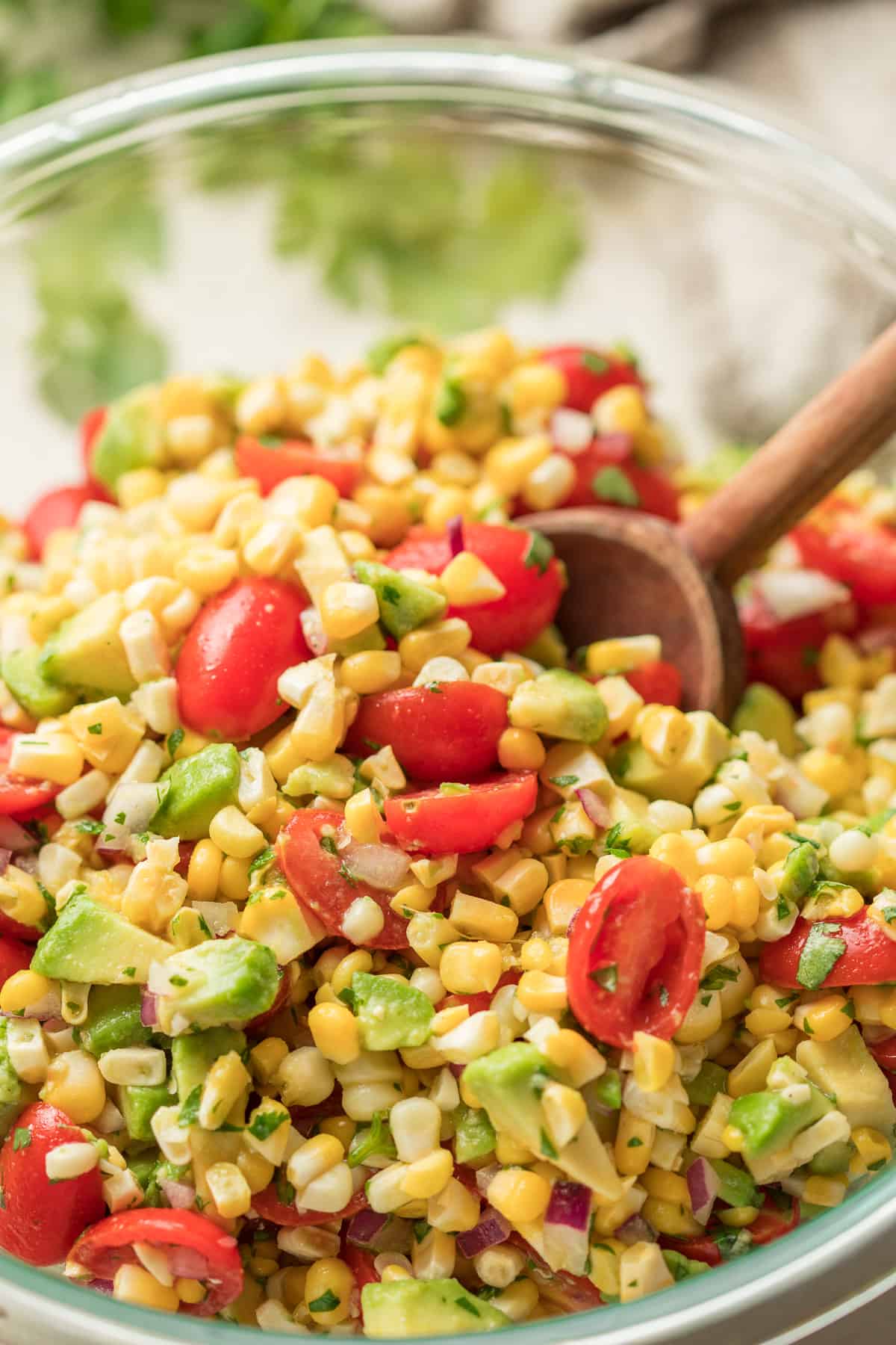Close Up of Avocado Corn Salad in a Bowl with Wooden Spoon