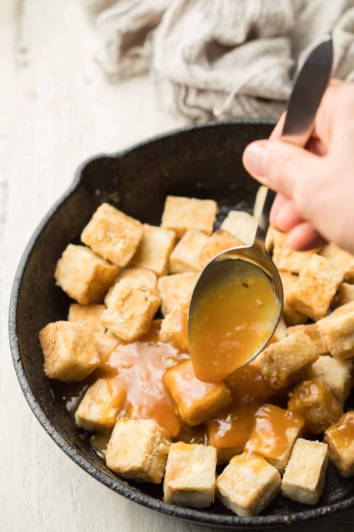 Hand Drizzling Orange Sauce Over a Skillet of Tofu