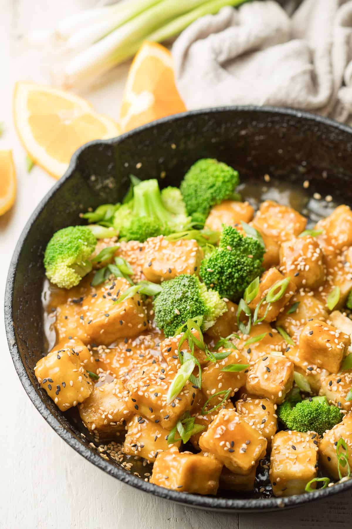 Skillet of Crispy Orange Tofu and Broccoli with Orange Slices in the Background