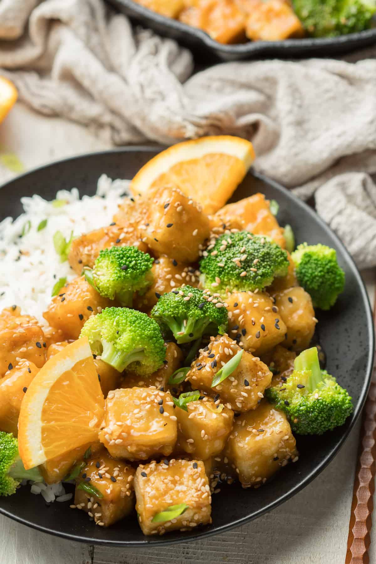 Plate of Crispy Orange Tofu, Broccoli, and Rice with Cloth and Skillet in the Background