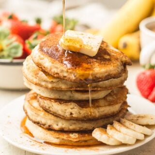 Hand Drizzling Maple Syrup Over a Stack of Vegan Banana Pancakes