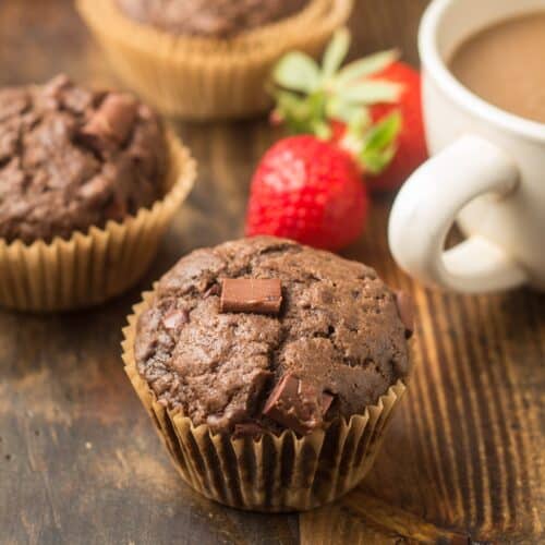 Vegan Double Chocolate Muffins on a Wood Surface with Coffee Cup, Strawberries and Additional Muffins in the Background