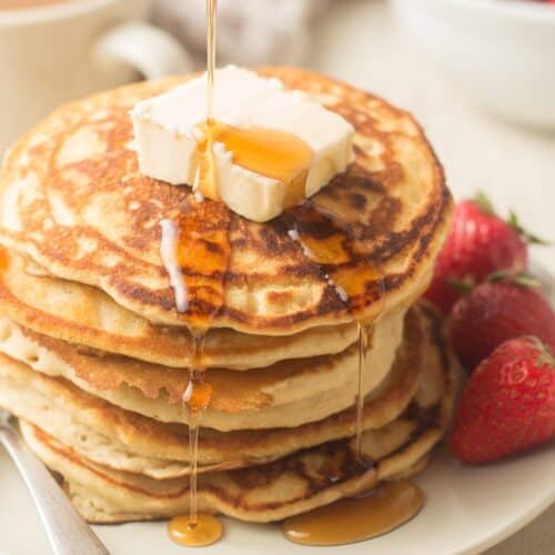 Syrup Being Poured Over a Stack of Vegan Pancakes with Butter and Strawberries