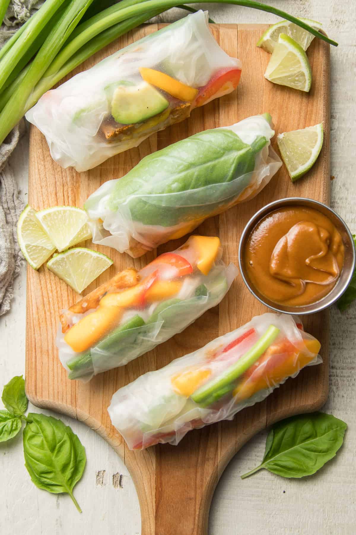 Vegan Summer Rolls on a Cutting Board with Lime Slices and a Dish of Peanut Sauce