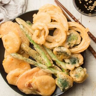 Tempura Vegetables on a Black Plate with Chopsticks and Dipping Sauce on the Side