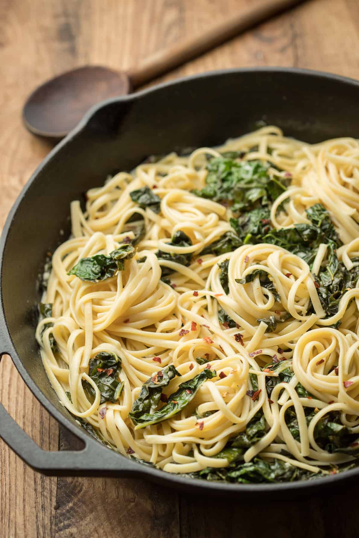 Creamy Kale Pasta in a Skillet with Wooden Spoon in the Background