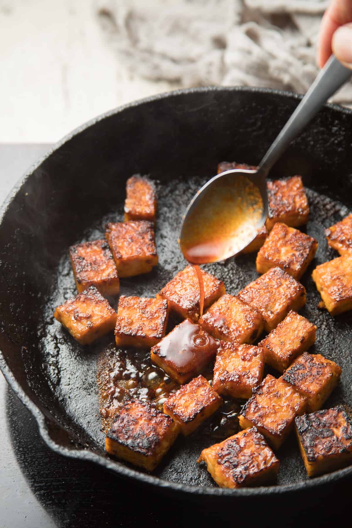 Spoon drizzling marinde over tempeh in a skillet.
