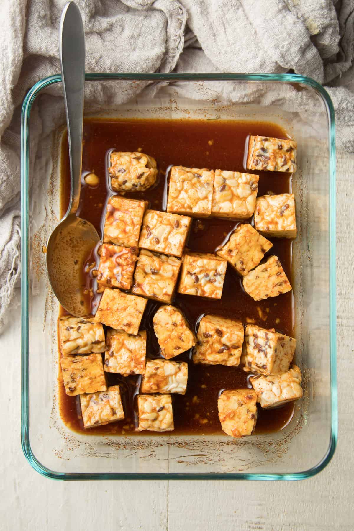 Tempeh marinating in a glass dish with spoon.