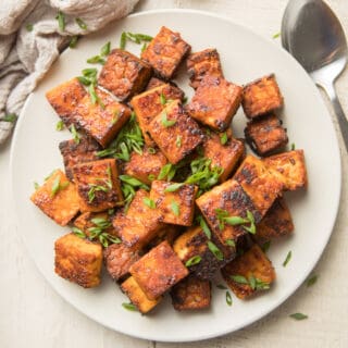 Plate of Smoky Marinated Tempeh with Chives on Top and Spoon on the Side.