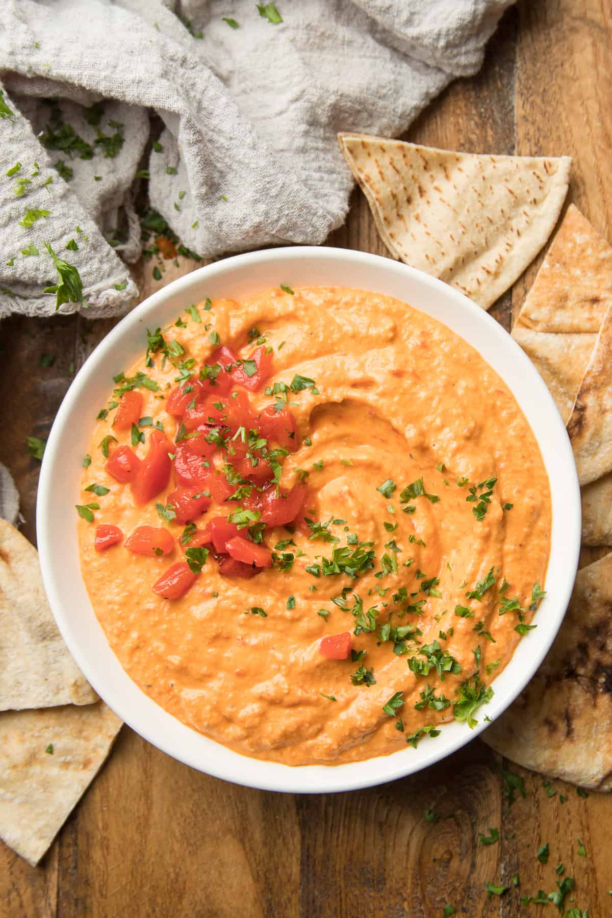 Bowl of Roasted Red Pepper Hummus on a Wooden Surface with Pita Wedges