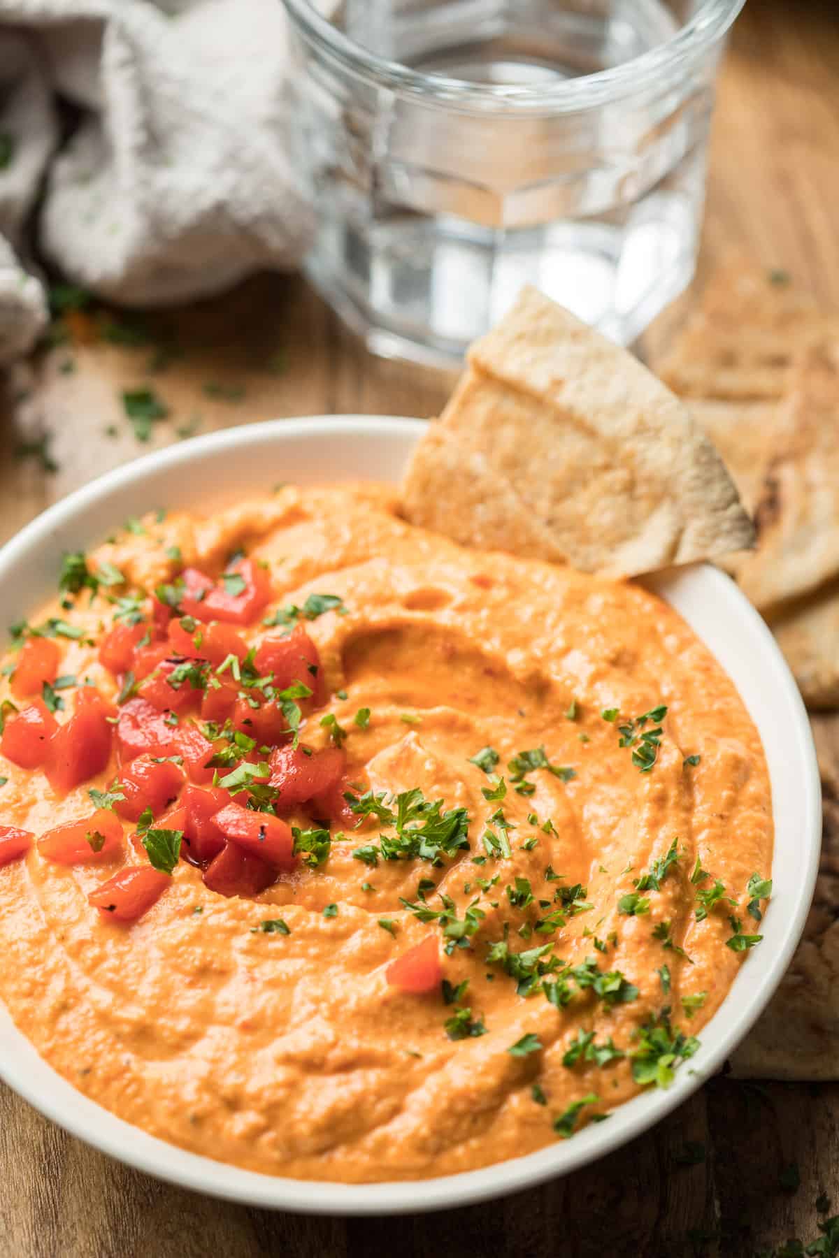 Bowl of Roasted Red Pepper Hummus with Pita Bread and Water Glass in the Background