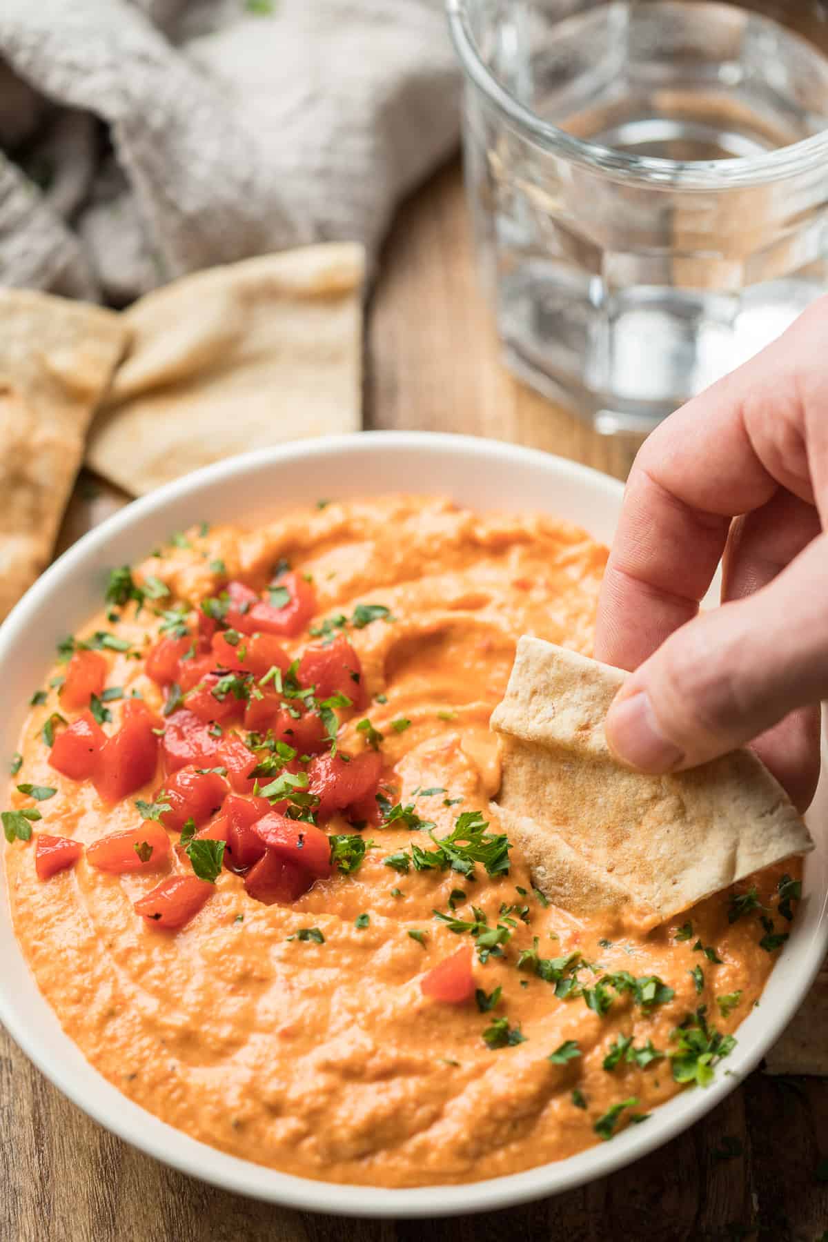 Hand Dipping a Pita Wedge into a Bowl of Roasted Red Pepper Hummus