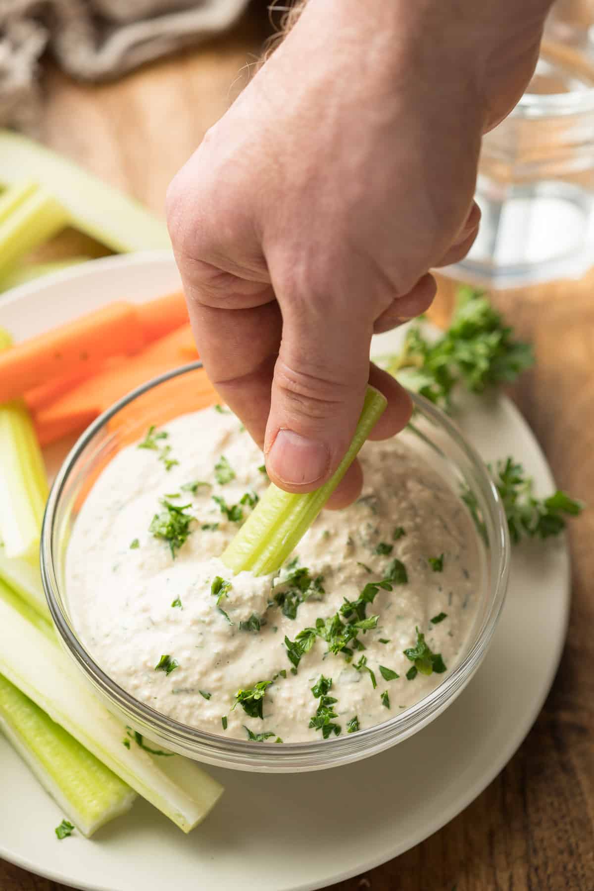 Hand Dipping a Celery Stick into a Bowl of Vegan Blue Cheese Dressing