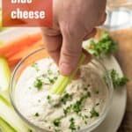Hand Dipping a Celery Stick into a Bowl of Vegan Blue Cheese Dressing with Text Overlay Reading "Vegan Blue Cheese"