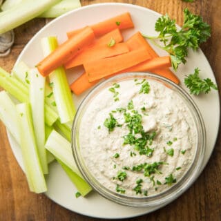 Bowl of Vegan Blue Cheese Dressing Surrounded By Carrot and Celery Sticks